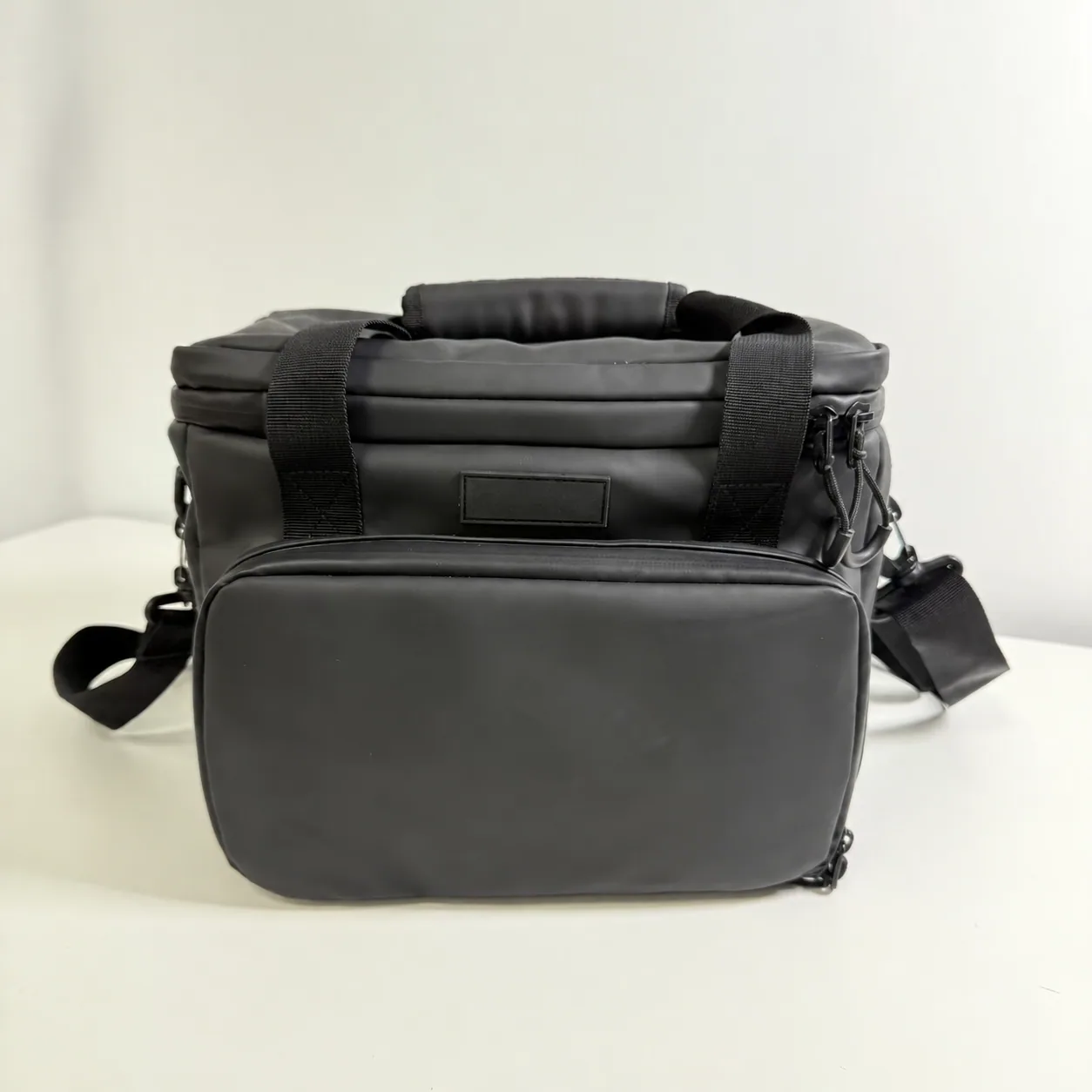 Actual black soft cooler sample with padded top handle, two front webbing handles and a large zippered front pocket; customer logo removed